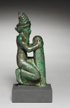 an ancient statue is sitting on a gray base and has a green pattered finish