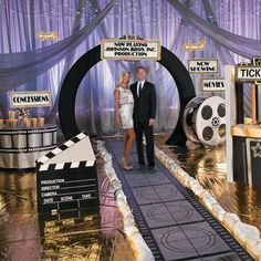 a man and woman standing in front of a stage set for a movie event with signs on it