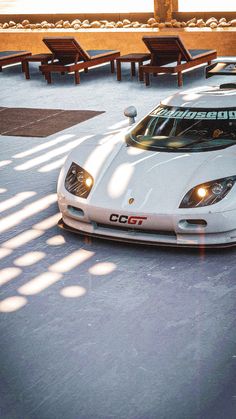 a white sports car is parked in the parking lot next to some benches and tables