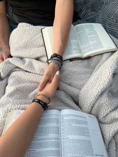 two people holding hands over an open book on top of a bed covered in blankets