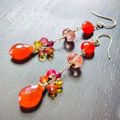 Gold filled statement earrings in stunning vibrant fiery red and orange hues. They are created with beautiful, exquisite quality carnelian briolettes and coins, petite coins of deep red garnet and delicately colored, plump in size, peach sapphire roundels wrapped in gold filled wire and arranged into attractive, long dangles. They are further embellished with small clusters of colorful sapphires above the carnelian briolettes.  Completed with gold filled ear wires these earrings measure 2.75 inches top to bottom. Perfect gift to brighten any occasion. Thank you for looking! Please contact me if you have any questions or requests. Free domestic First Class shipping. Shipping upgrade available. Gift wrap included and always free. Follow Agusha on Instagram @channahmorgenstern and Facebook: w Orange Gemstone Dangle Earrings, Orange Gemstone Drop Earrings, Party Red Gemstone Earrings, Red Gemstone Earrings For Valentine's Day, Orange Dangle Earrings With Natural Stones, Red Wire Wrapped Drop Earrings, Red Wire Wrapped Dangle Earrings, Orange Natural Stones Drop Earrings, Bohemian Red Gemstone Earrings