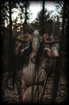 a woman with long hair and makeup standing in the woods, covering her face with fabric