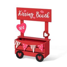 a red wooden bench with hearts and bunting on the top, sitting in front of a sign that says kissing booth