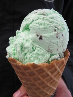 a person holding an ice cream cone with mint green icing and chocolate sprinkles