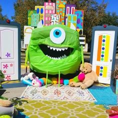 a large green monster sitting on top of a colorful rug next to stuffed animals and toys