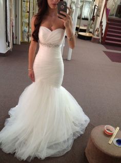 a woman in a white wedding dress taking a selfie with her cell phone and looking at the camera