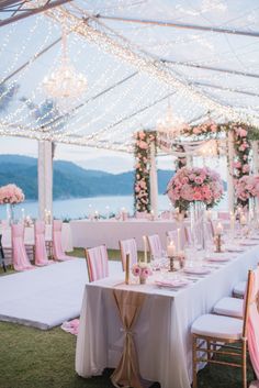 an outdoor wedding reception setup with pink and white flowers on the tables, chandeliers and candles