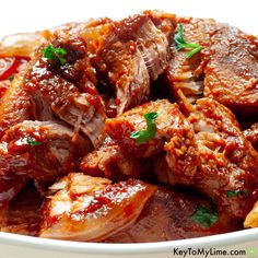 a bowl filled with meat covered in sauce and garnished with parsley on top