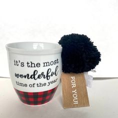 a cup with a black pom - pom sitting next to it's tag