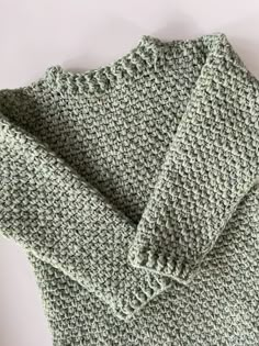 a green knitted sweater laying on top of a white surface