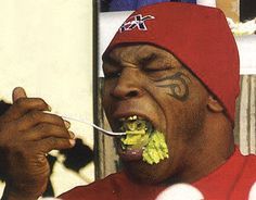 a man with his mouth open eating broccoli while wearing a red beanie