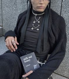 a person sitting on the ground wearing glasses and holding a book in their hand with chains around his neck