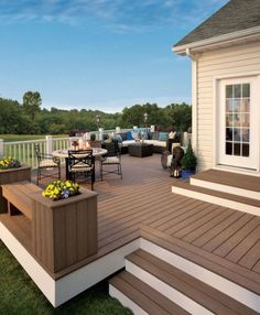 a deck with chairs, tables and potted plants on the side of it in front of a house