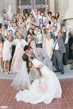 a bride and groom kissing in front of a large group of people