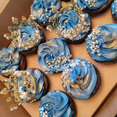 cupcakes decorated with blue frosting and pearls are in a box on the table