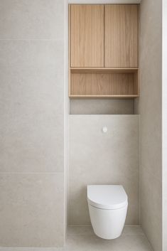 a white toilet sitting inside of a bathroom next to a wooden shelf on the wall