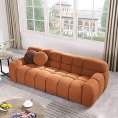 an orange couch sitting in front of a window next to a table with fruit on it