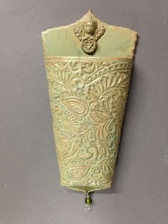 a green vase hanging from the side of a wall with a metal hook on it