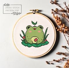 a cross stitch frog sitting on top of a plant