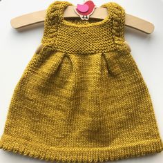 a yellow knitted dress with a pink bird on the front and bottom, hanging from a wooden hanger