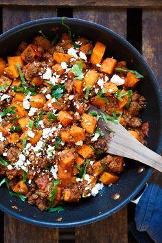 a skillet filled with meat and vegetables on top of a wooden table next to a blue towel