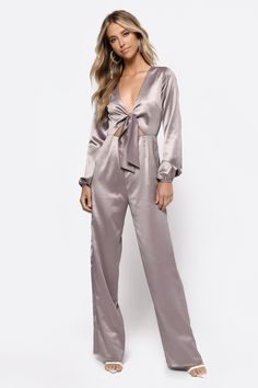 This Satin Jumpsuit Is Looking To Party. The Mila Taupe Front Tie Satin Jumpsuit Features Long Relaxed Sleeves, V-Neckline, Front Tie, Front Cut Out, And Flared Legs. This Flare Leg Jumpsuit Will Look Great With An Up-Do And Statement Earrings At Your Next Soiree. Satin Jumpsuit Outfit, Jumpsuits For Women Indian, Jumpsuit Outfit Casual, Flare Leg Jumpsuit, Trendy Jumpsuit, Jeans Overall, Satin Jumpsuit, Silk Jumpsuit, Jumpsuit Outfit