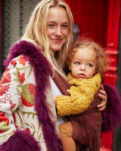 a woman holding a child in her arms and smiling at the camera while walking down the street