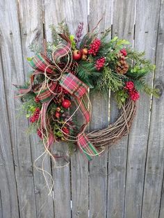 a christmas wreath hanging on the side of a wooden fence with berries and greenery