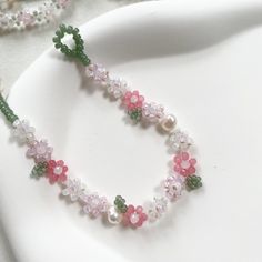 a white plate topped with pink and green beaded necklace next to a string of pearls