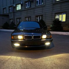 a black car parked in front of a building at night with its headlights turned on