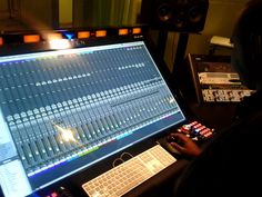 a man sitting in front of a computer monitor with sound mixing equipment behind him on the desk