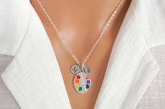 Antique silver plated and enamel paint palette / pallet necklace. It comes with a personalized initial and birthstone charm. This necklace includes: - painter's palette charm (size 30 mm | 1 1/8 inch) - initial charm - Preciosa Elements birthstone charm - antique silver anchor chain (14 to 36 inches) To Add Initial or Number Charms: https://etsy.me/3RnJ5qD  To Add Birthstone Charms: https://etsy.me/3Zif2Uw Looking for more jewelry? Visit our shop: https://cppewter.etsy.com ♥ SHIPPING INFO ♥ We s