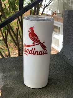 a white tumbler with a red cardinal logo on it sitting on a stone bench