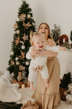 a woman holding a baby in front of a christmas tree