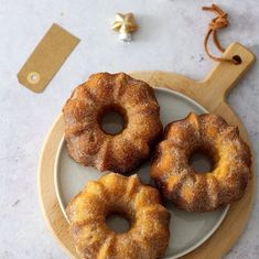 three donuts sitting on top of a white plate next to a wooden cutting board