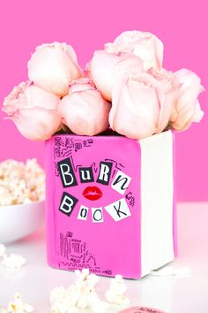 a pink box filled with white flowers next to a bowl of popcorn