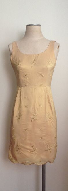 "Very classic and elegant 1960's gold cocktail dress with machine embroidered flowers and scalloped hem is a lightweight taffeta and is fully lined. Sleeveless dress zips up the back and also has a small kick pleat for extra movement on the dance floor! The dress is in excellent condition save for a small stain under a chest pleat(see pic). Sold as is. Fabric -taffeta Lining - acetate Chest 32\" Waist 23\" Hips 35\" Vintage garments have been previously worn and lovingly cared for, they may howe Gold Sheath Dress For Spring, Spring Wedding Dress With Gold Embroidery, Gold Silk A-line Dress, Gold Sleeveless Silk Dress, Gold Silk Sleeveless Dress, Gold Silk Dress With Gold Embroidery, Gold Floral Embroidery Evening Dress, Fitted Embroidered Gold Dress, Spring Dresses With Gold Embroidery