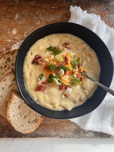 a bowl of soup with bacon, cheese and bread on a wooden table next to a napkin