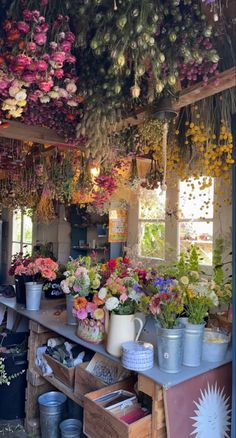 a room filled with lots of potted plants and flowers hanging from the ceiling above