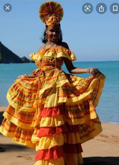 a woman is standing on the beach in a colorful dress and headdress,