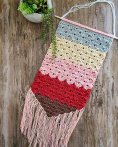 a multicolored crocheted bag hanging on a wooden wall next to a potted plant