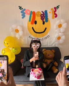 a woman sitting on top of a couch holding a cell phone next to a cake