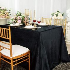 a black table cloth with white chairs and flowers on the side is set up for a formal dinner