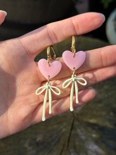 Pink heart resin earrings with cream coloured bows, hung on gold plated huggies Cute Earrings With Pink Bow For Gift, Cute Pink Bow Earrings As Gift, Cute Pink Bow Earrings For Gift, Pink Heart-shaped Jewelry With Bow, Heart-shaped Earrings With Bow For Gift, Cute Bow Jewelry For Valentine's Day, Heart-shaped Bow Jewelry For Valentine's Day, Bow Earrings For Valentine's Day Gift, Feminine Heart Charm Earrings For Gift