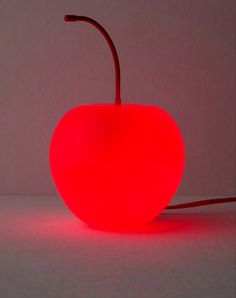 a red apple shaped lamp sitting on top of a white table next to a gray wall