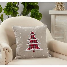 a christmas tree pillow sitting on top of a chair next to a potted plant