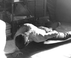 a shirtless man laying on the floor in front of a stack of books