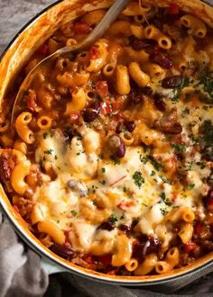 a large pot filled with pasta and sauce on top of a table next to a spoon