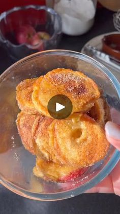 a person holding up a bowl filled with doughnuts on top of a table