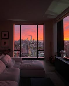 a living room filled with furniture and large windows overlooking the city at sunset or dawn